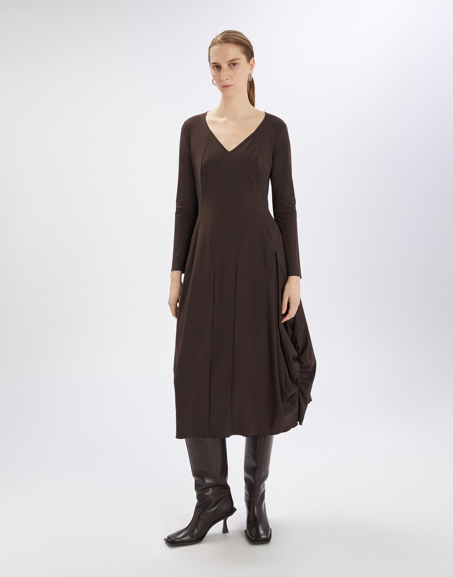 Frontalansicht: Eine Frau trägt das AT-LENGTH Kleid, ein dunkelbraunes, langärmeliges, knielanges Ballonkleid mit V-Ausschnitt und seitlichen Raffungen.
