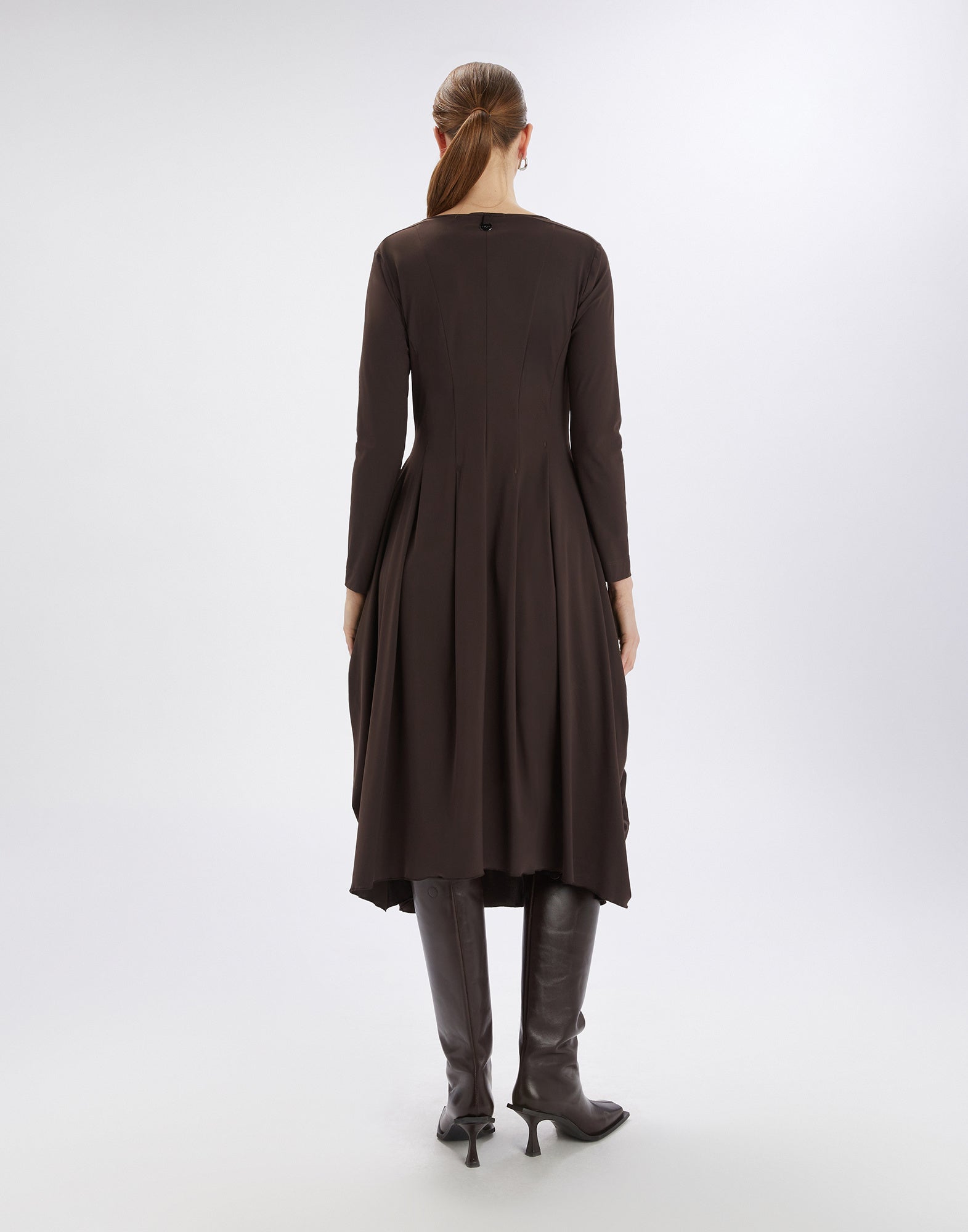 Rückansicht eines knielangen, dunkelbraunen AT-LENGTH Kleides mit langen Ärmeln, Falten und ballonförmigem Saum, getragen von einer Frau mit Stiefeln.