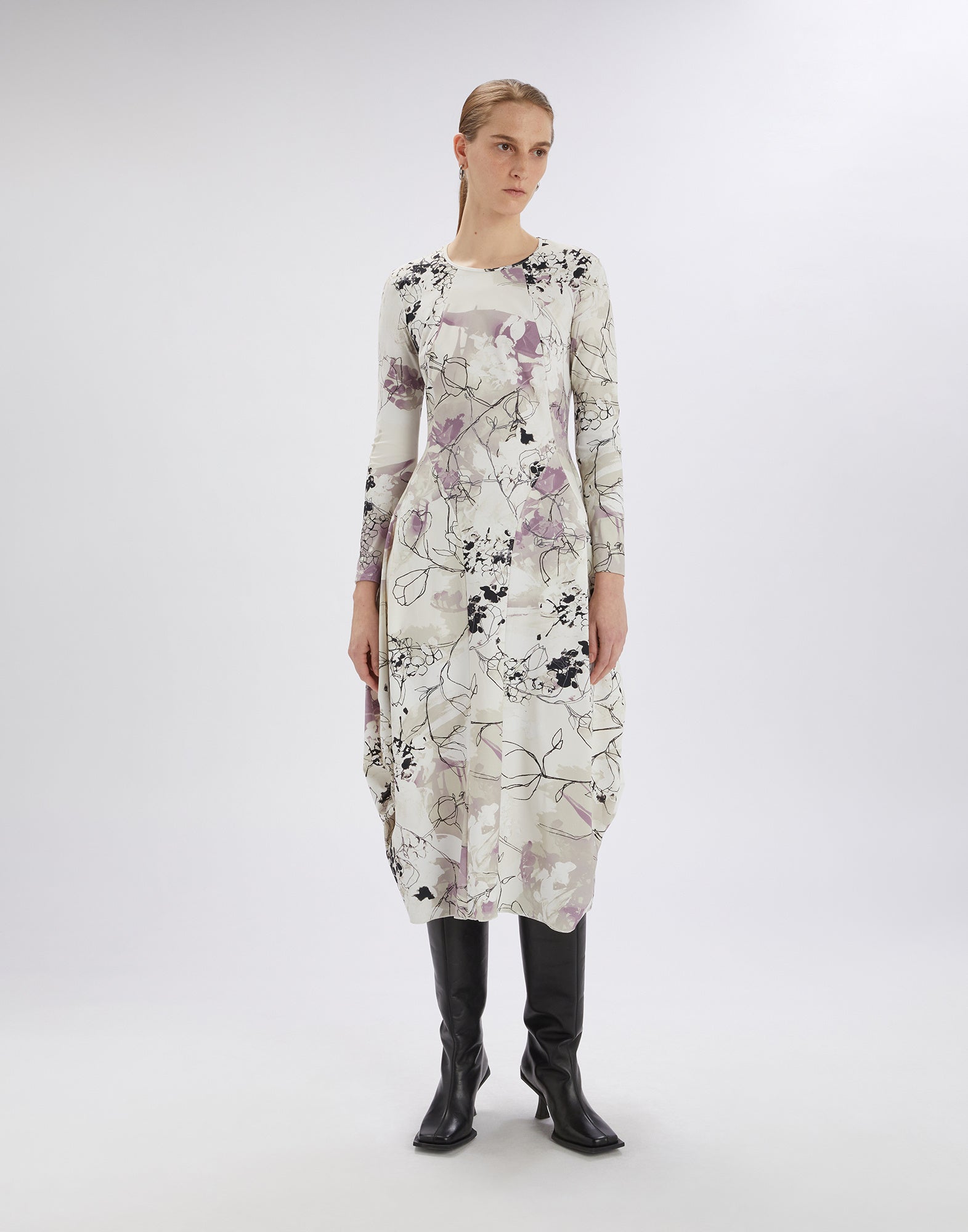 Frontalansicht: Modell trägt das AT-LENGTH Kleid mit langem Ärmel, Ballonform und Layered Flowers-Druck, kombiniert mit schwarzen Stiefeln in hellem Fotostudio.