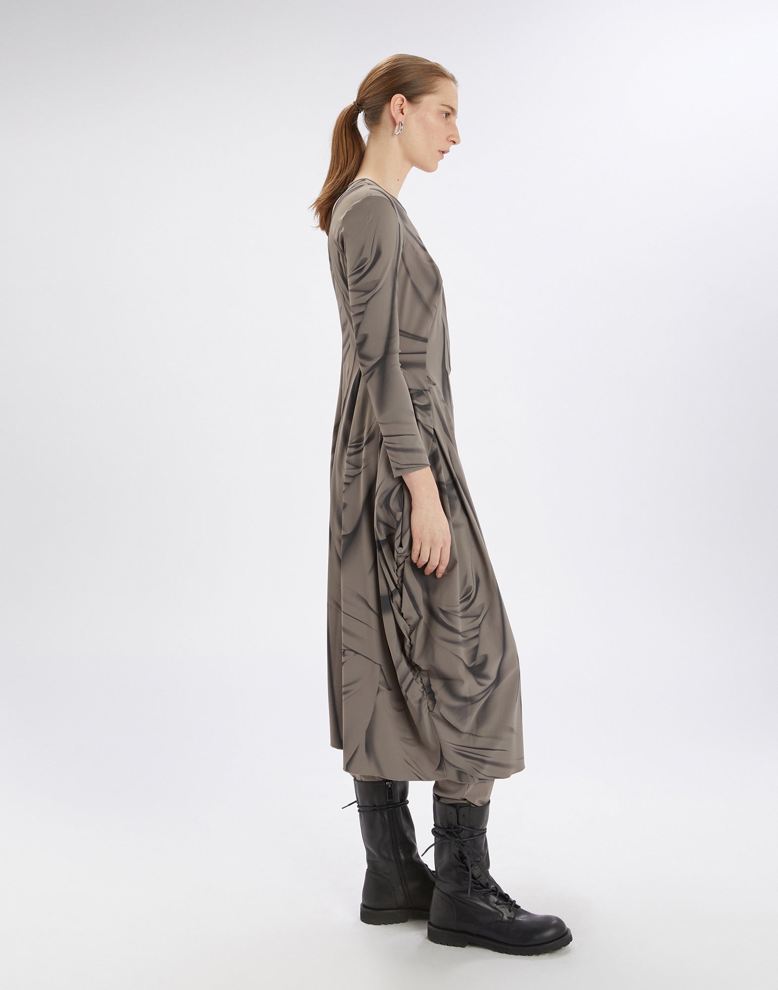 Side view of a model in the AT-LENGTH dress with long sleeves, balloon shape, and Drapery print, paired with black boots, against a neutral background.