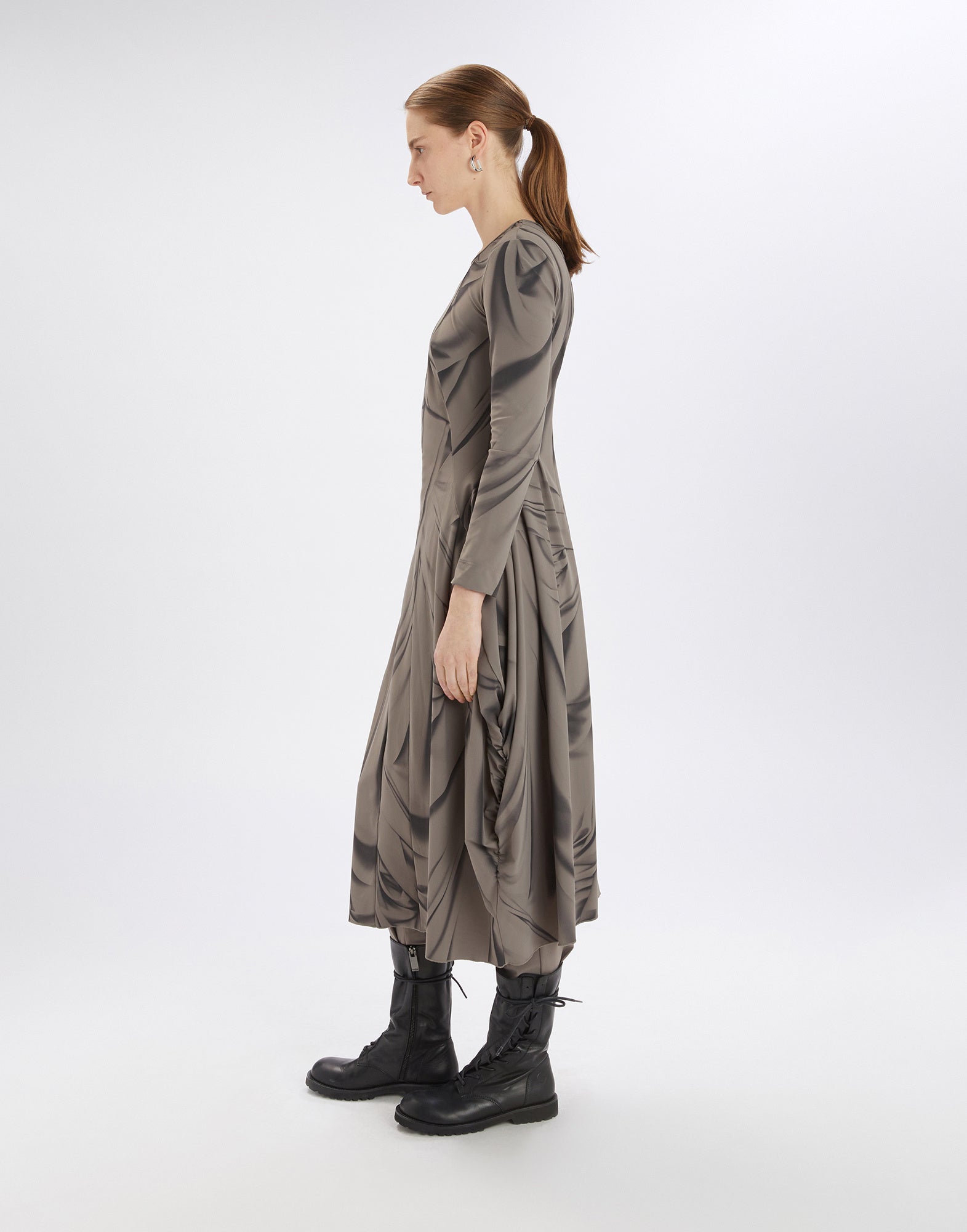 Side view of a woman in the AT-LENGTH dress with print, long sleeves, balloon-shaped skirt, side gathering, and black boots against a white background.