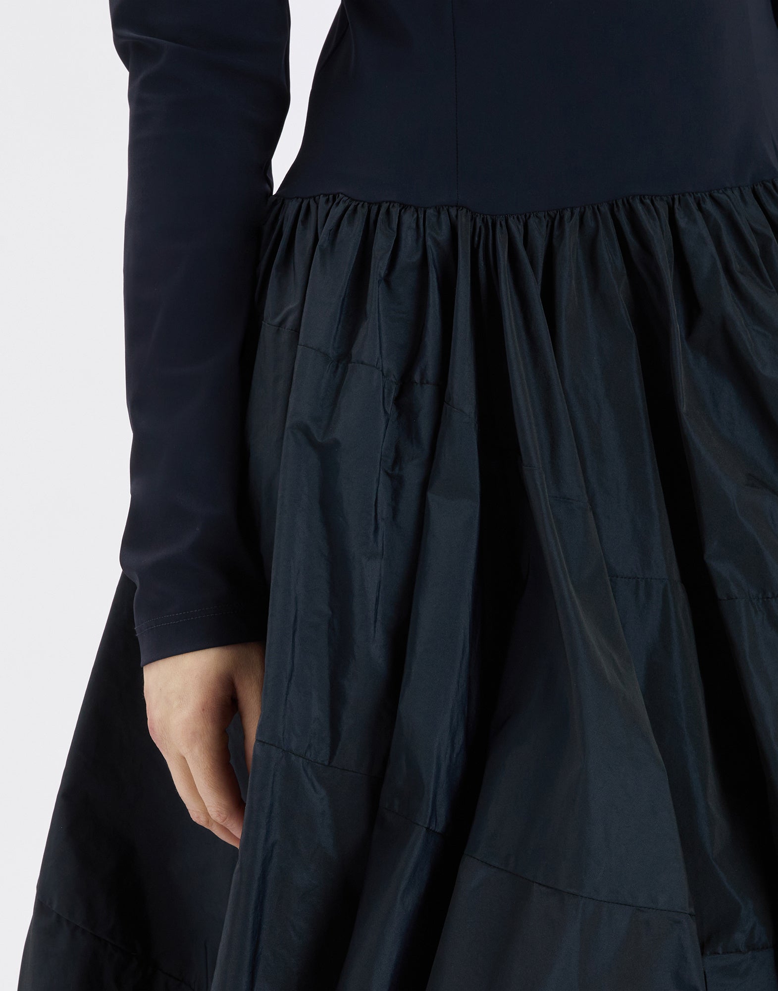 Detailansicht vom unteren Teil des GRID Kleides mit Ballon-Effekt, glattem Taft und körpernahem, langärmligem Oberteil, sichtbare Hand am Saum.