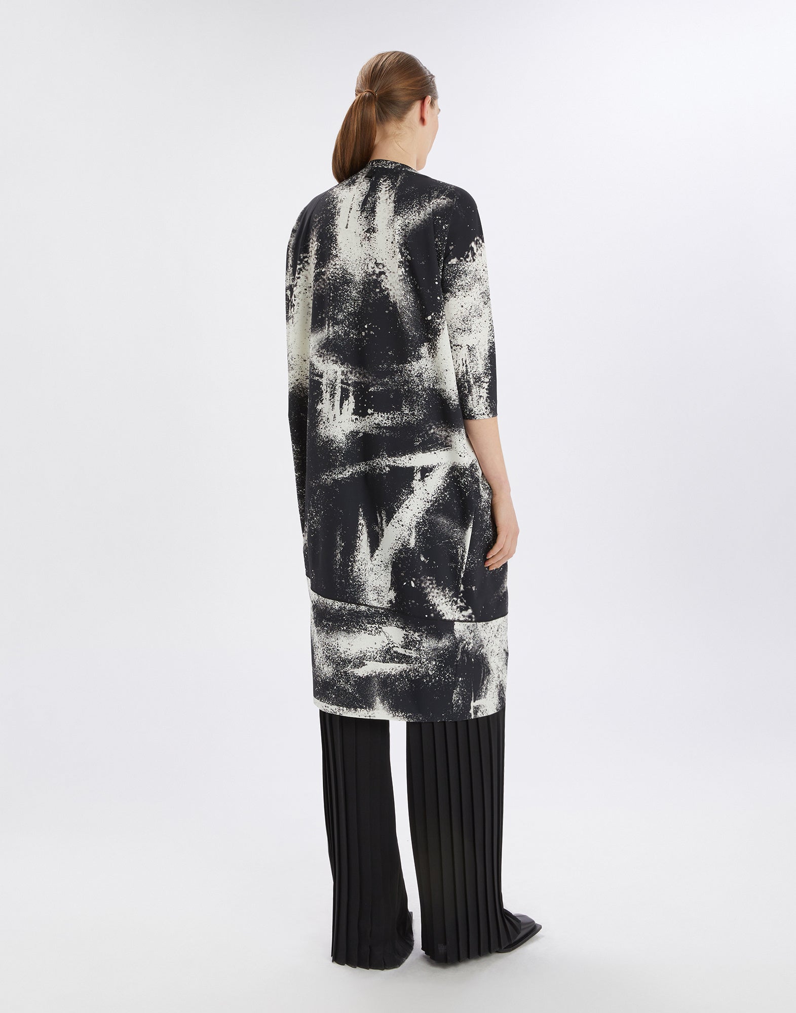 Rear view of a person wearing the PRELUDE dress with black-and-white spray-effect print, three-quarter sleeves, and asymmetric hem.