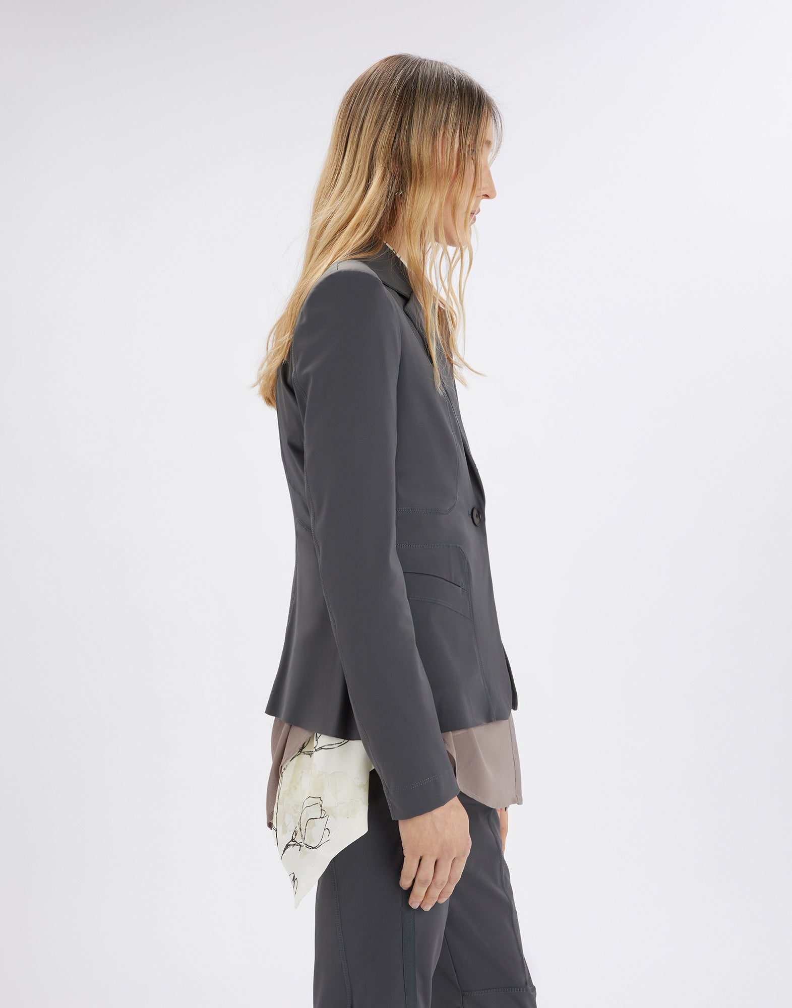 Side view of a person wearing the tailored NO-WAY blazer made from compact scuba fabric in dark grey with visible seams and shoulder pads.
