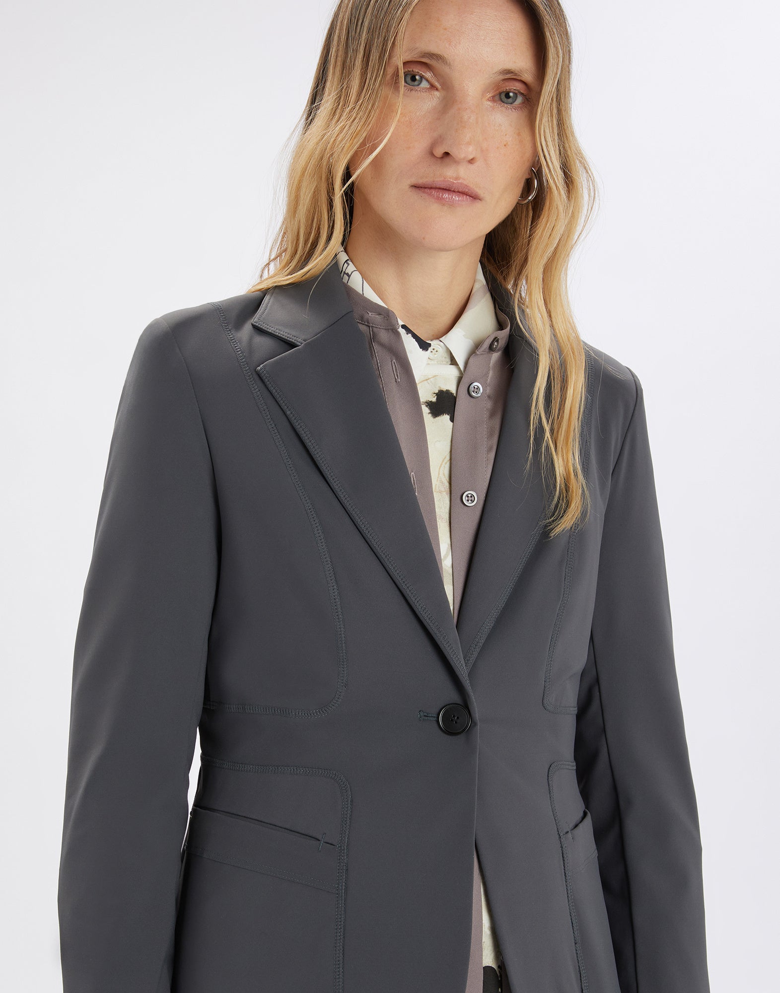 Front view of a woman wearing the NO-WAY blazer; the compactly knit dark gray scuba fabric features raw edges, visible seams, and a single-button closure.