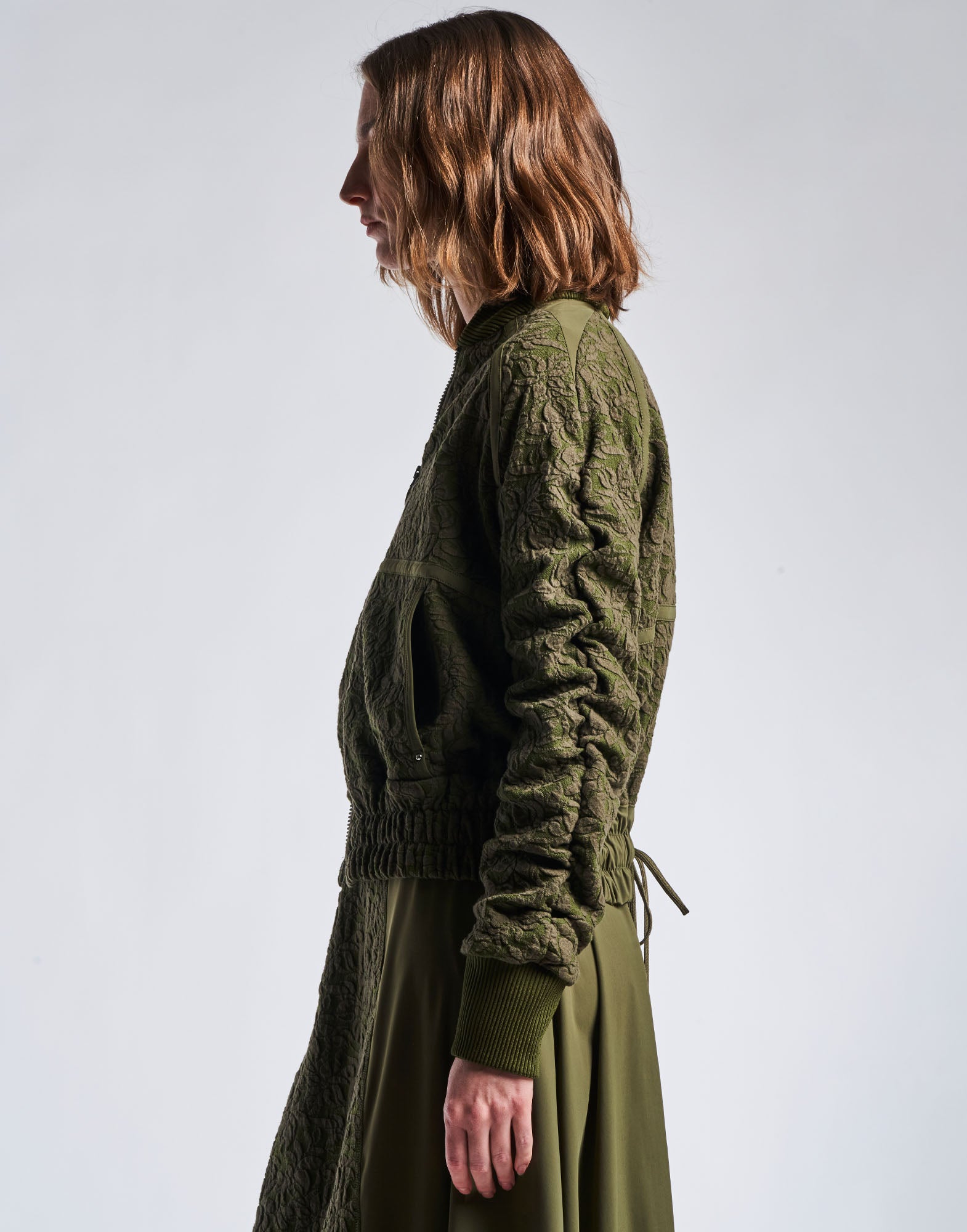 Side view of a person wearing the BOAST bomber jacket in floral jacquard cotton mix and military green nylon, featuring visible ruching on raglan sleeves, wide elastic waistband, and ribbed cuffs.
