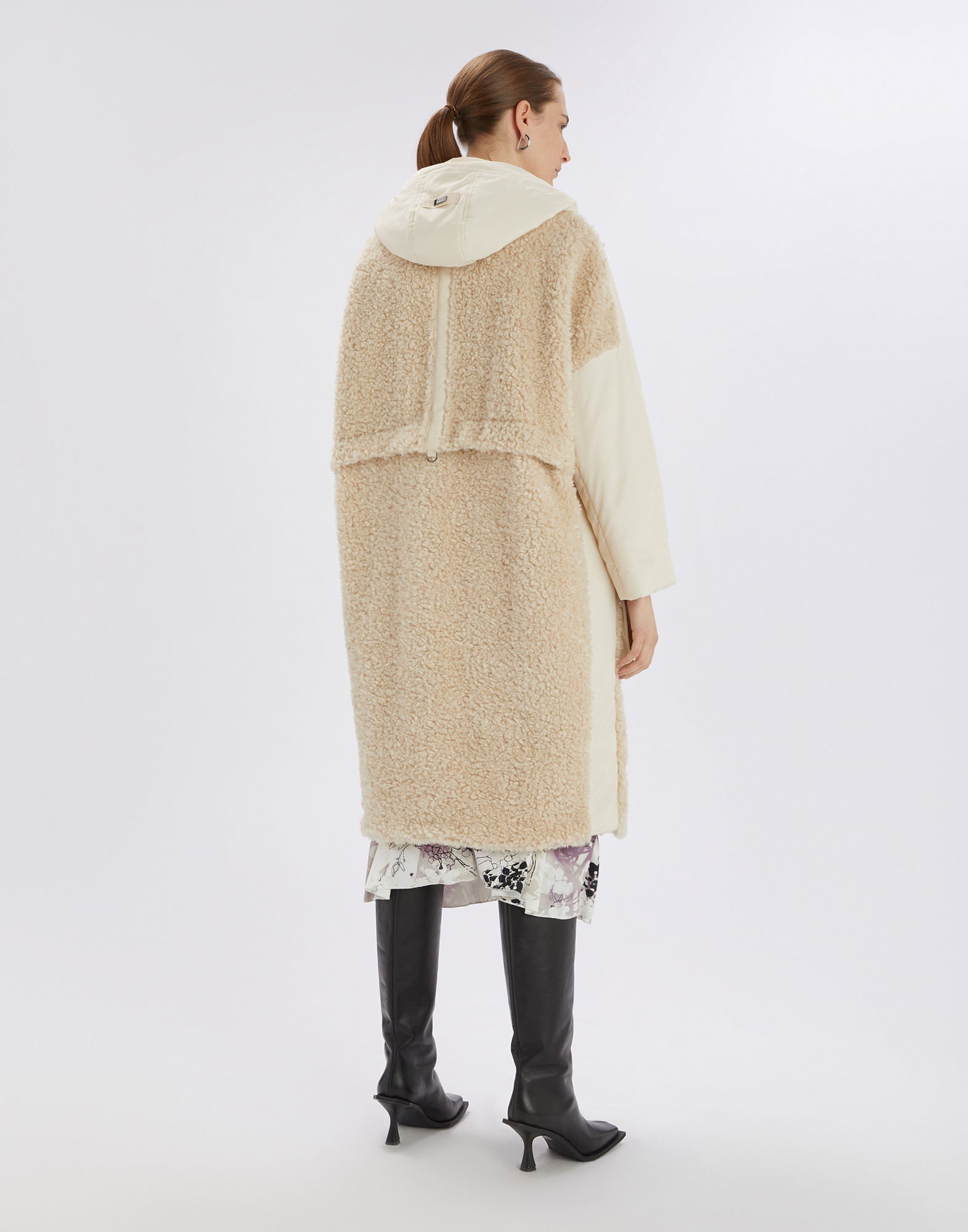 Rear view of knee-length, beige ANNOTATE coat made of sherpa fabric and nylon, with large hood and visible dividing seam, worn by a woman.
