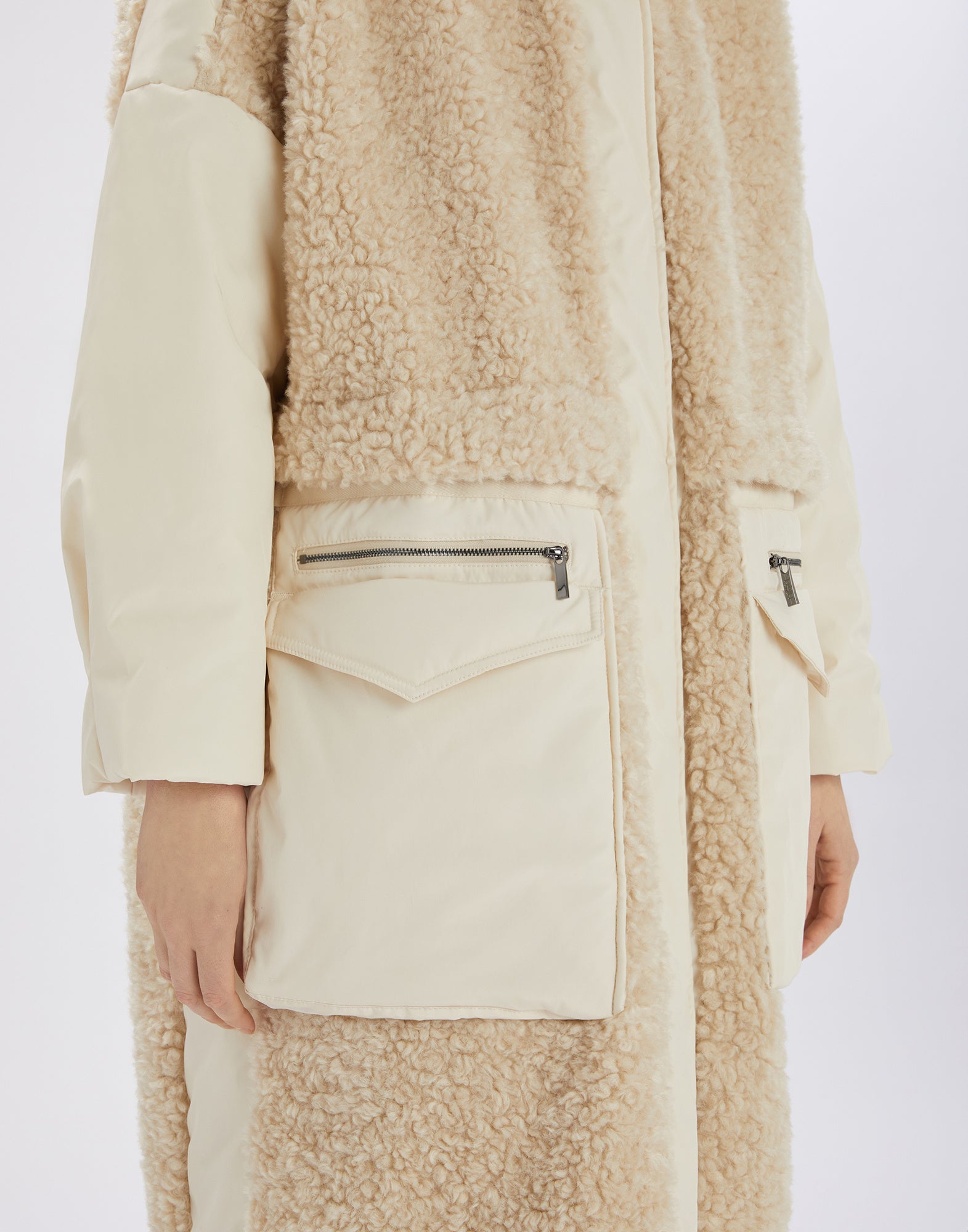 Detail view of the ANNOTATE coat, showing large front zip pockets, soft beige sherpa fabric, and nylon inserts from the front perspective.