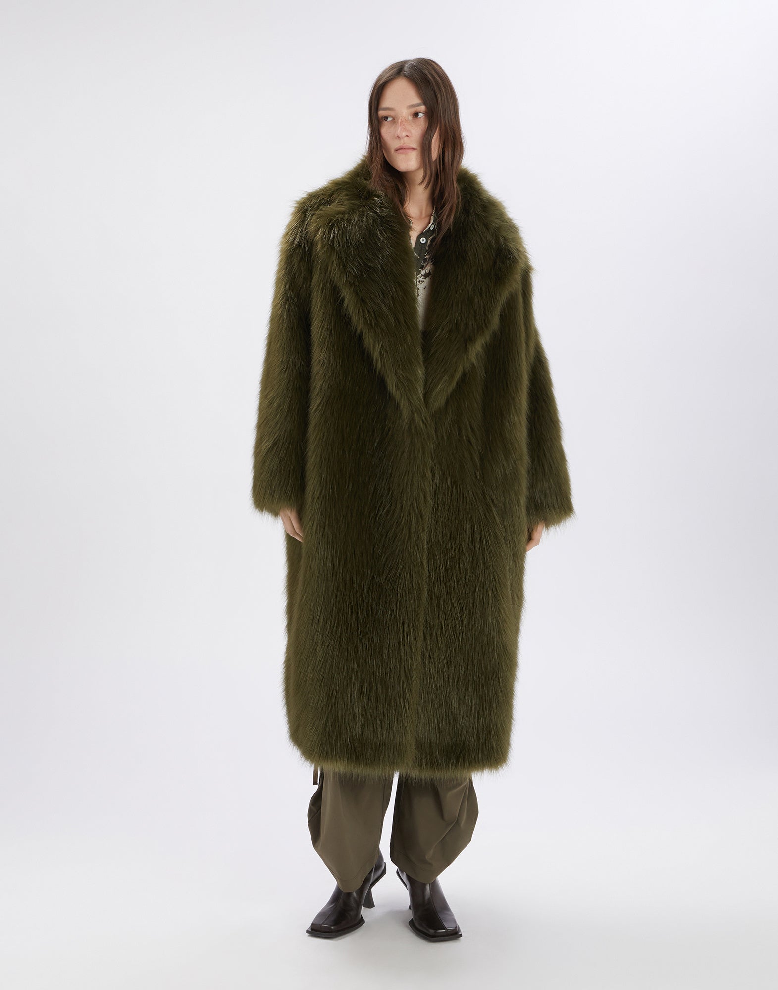 Frontalansicht: Person trägt CROSSING Kunstpelzmantel in Olivgrün mit Maxi-Volumen, breitem Reverskragen und Länge bis knapp über die Knöchel, luxuriös und dramatisch.