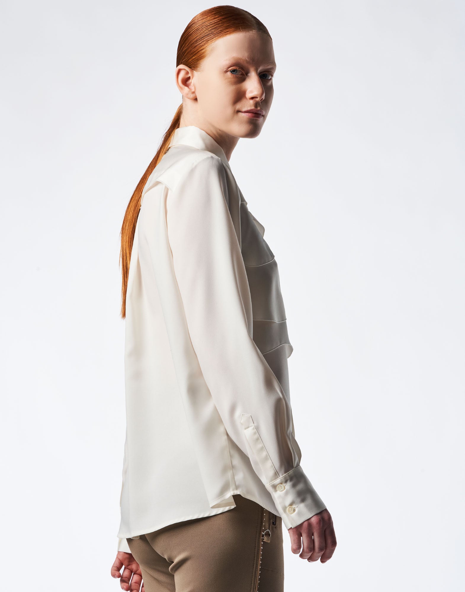 Side view of a woman wearing the ALTERNATE blouse. The blouse is made of lightweight matte and shiny crepe, features long sleeves and a turn-down collar.