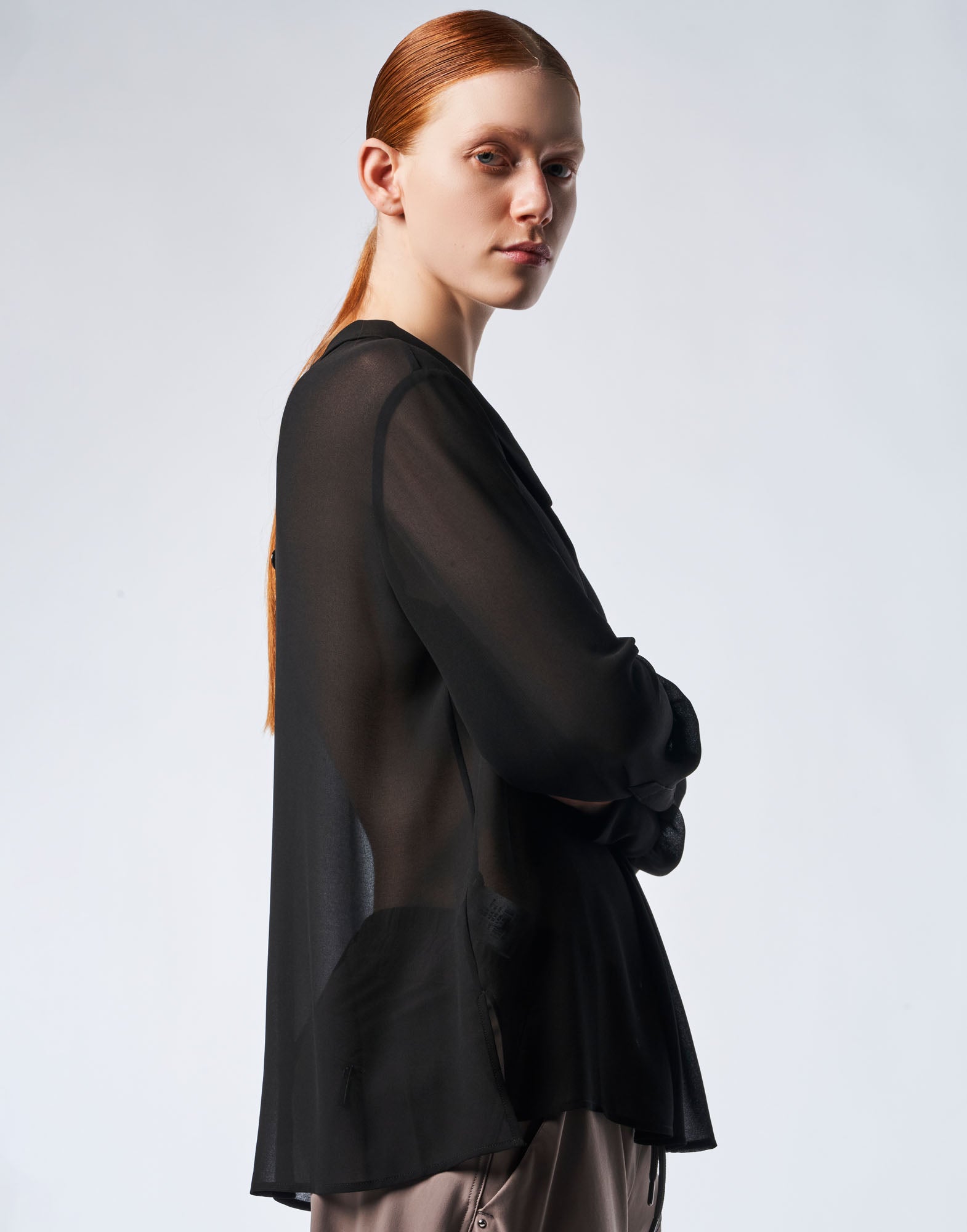 Seitenansicht: Modell trägt die VICE VERSA weite Bluse aus schwarzem, durchsichtigem Funktions-Georgette, mit weichem Klappkragen und langen Ärmeln.