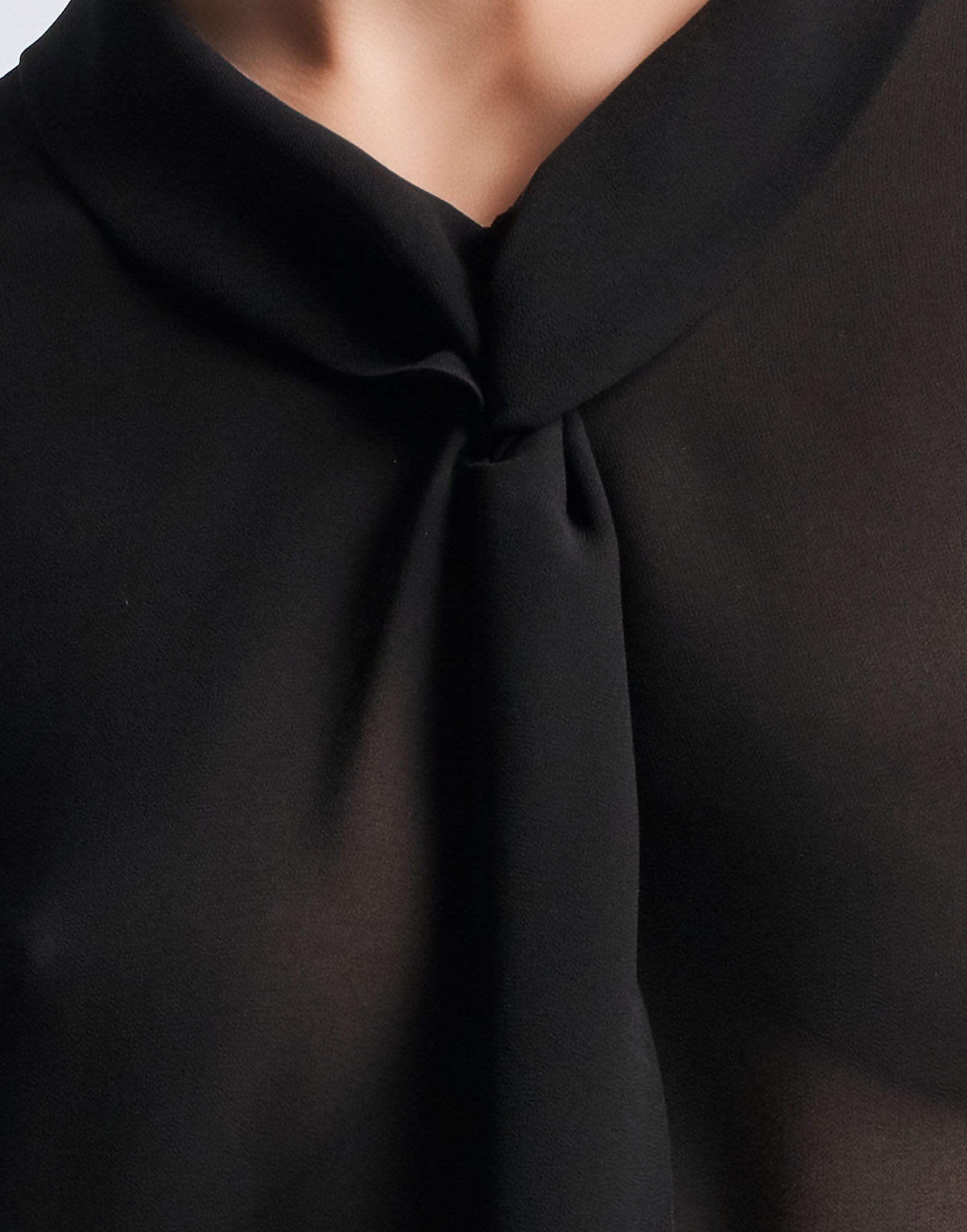 Detailansicht: VICE VERSA Bluse aus schwarzem, transparentem Funktions-Georgette, zeigt weichen Klappkragen mit Wickelkonstruktion und Drapierung am Ausschnitt.