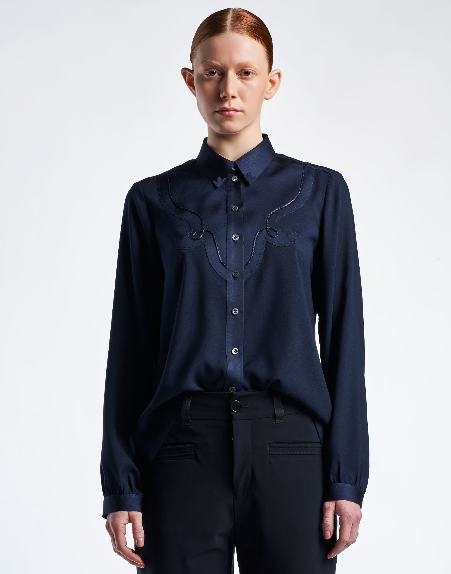 Frontalansicht einer Person, die die Bluse APPRECIATION im Westernstil trägt. Die Bluse hat matte und glänzende Seitenteile, einen Klappkragen und Perlmuttknöpfe. Verziert mit Zierkordel, doppelter Passe und Schnörkelmuster. Die Ärmel enden in Knopfmanschetten.