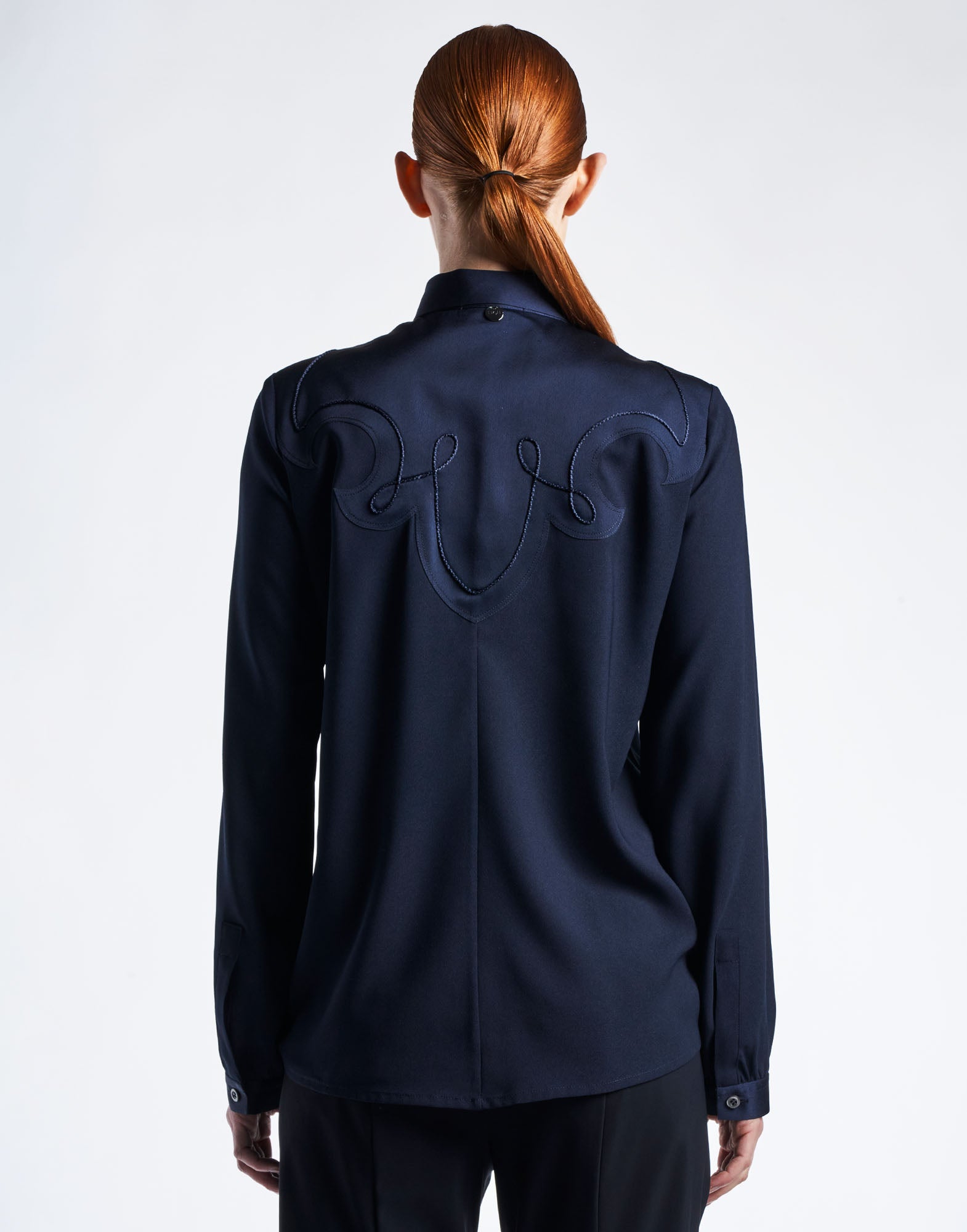 Rear view of a person wearing the APPRECIATION western-style blouse; colorful technical satin-back crepe with curlicue design and decorative cord over back and shoulders.