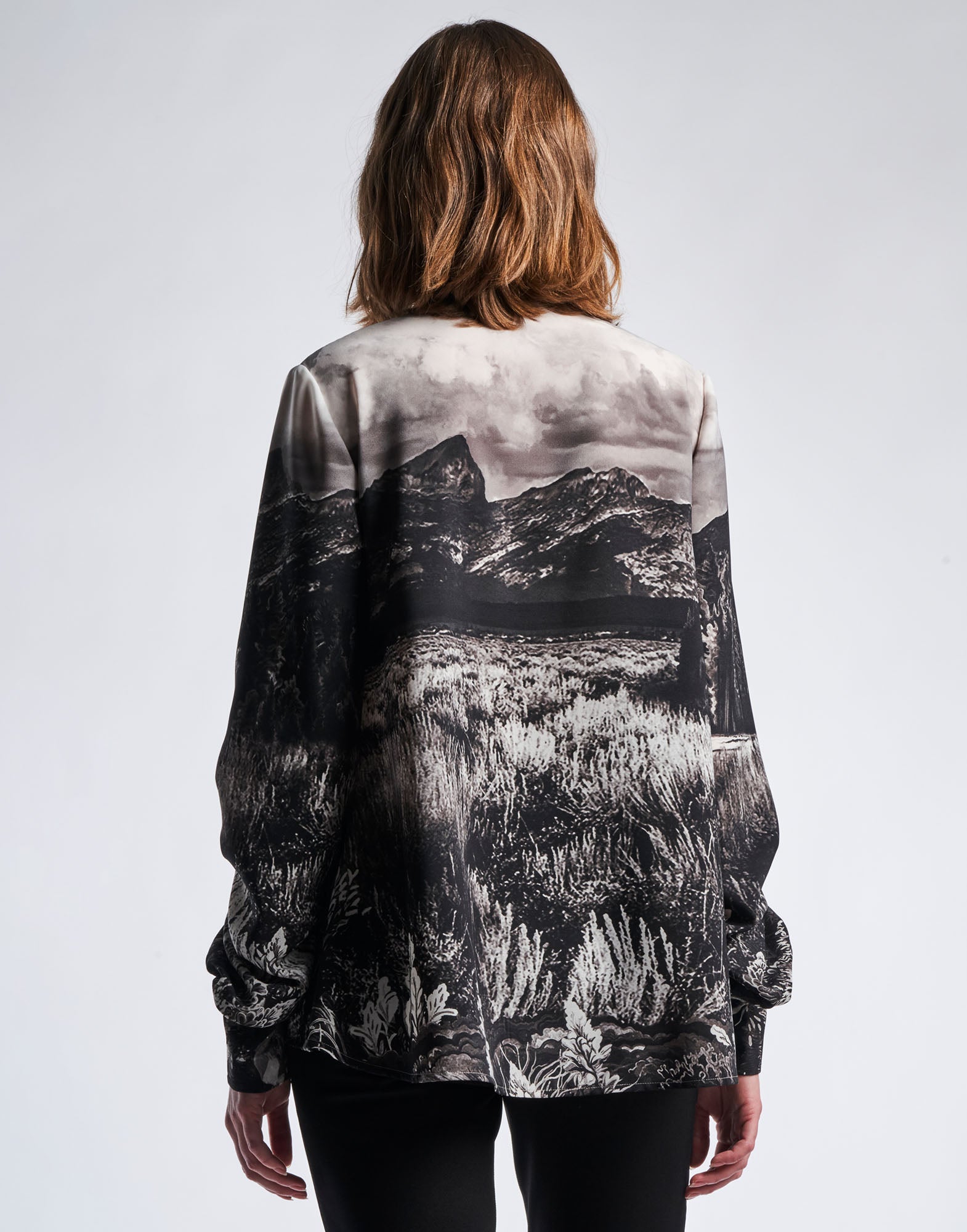 Back view of a person wearing the AMAZEMENT blouse with black and white 'Wyoming' print. The long sleeves and curved hem are clearly visible.