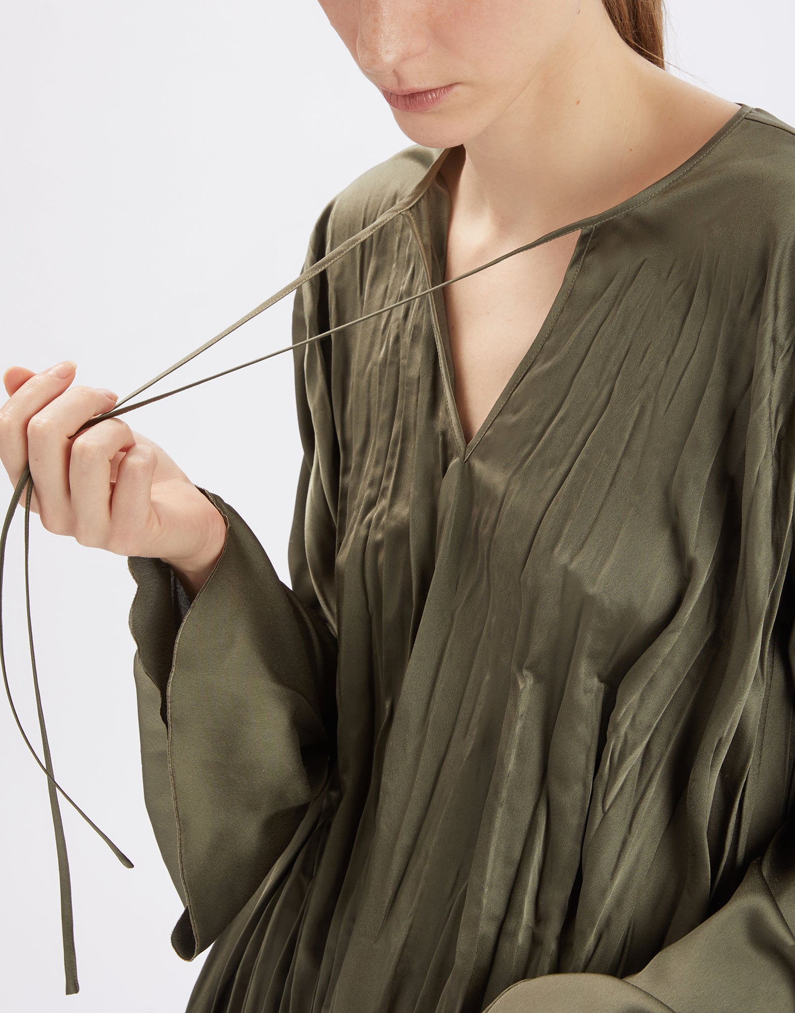 Detailansicht: Eine Person trägt die ONTOP Bluse in glänzendem, elastischem Satin. Sichtbar sind der große, runde Ausschnitt mit Kordeln, plissierte Struktur und weite Ärmel.