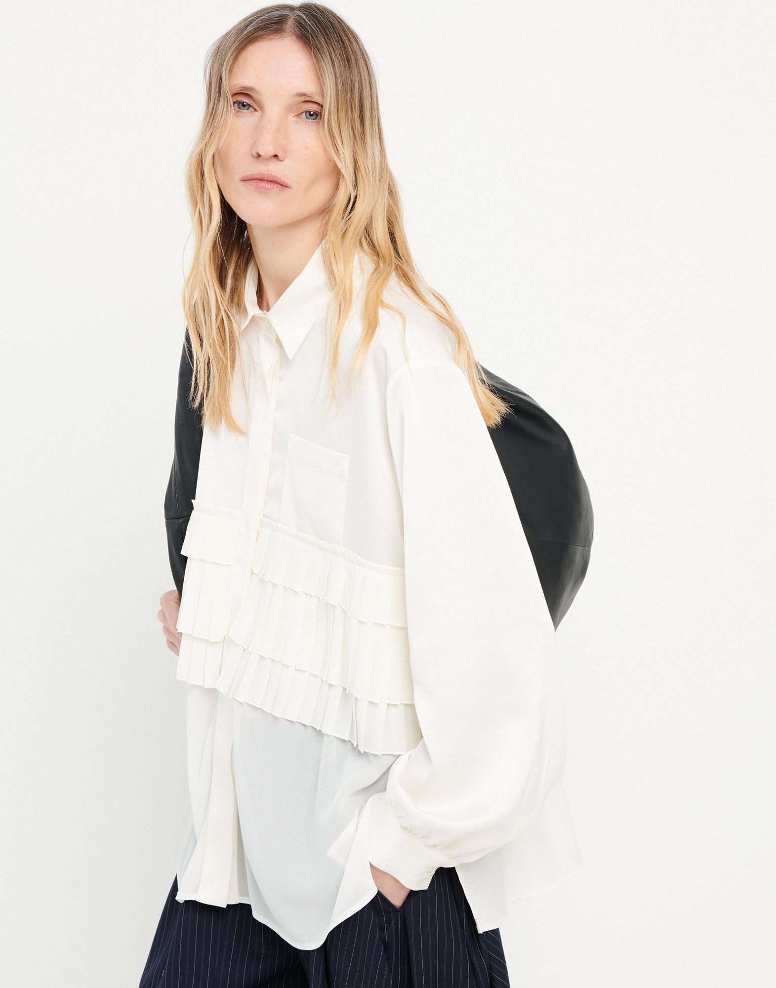 Frontalansicht der MERYL Bluse: Weiße Georgette-Bluse mit plissierten Volants am Oberkörper, Brusttasche, langen Ärmeln, umgeschlagenem Kragen und verdeckter Knopfleiste.