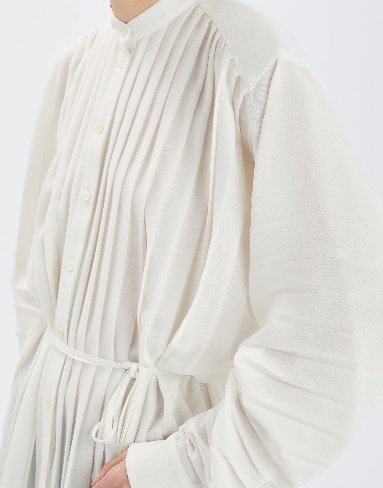 Frontalansicht der SLIM Bluse mit feinen Plisseefalten, Mao-Kragen, Knopfleiste und Kordelzug in gleicher Farbe, lange Ärmel mit Knopfmanschetten.