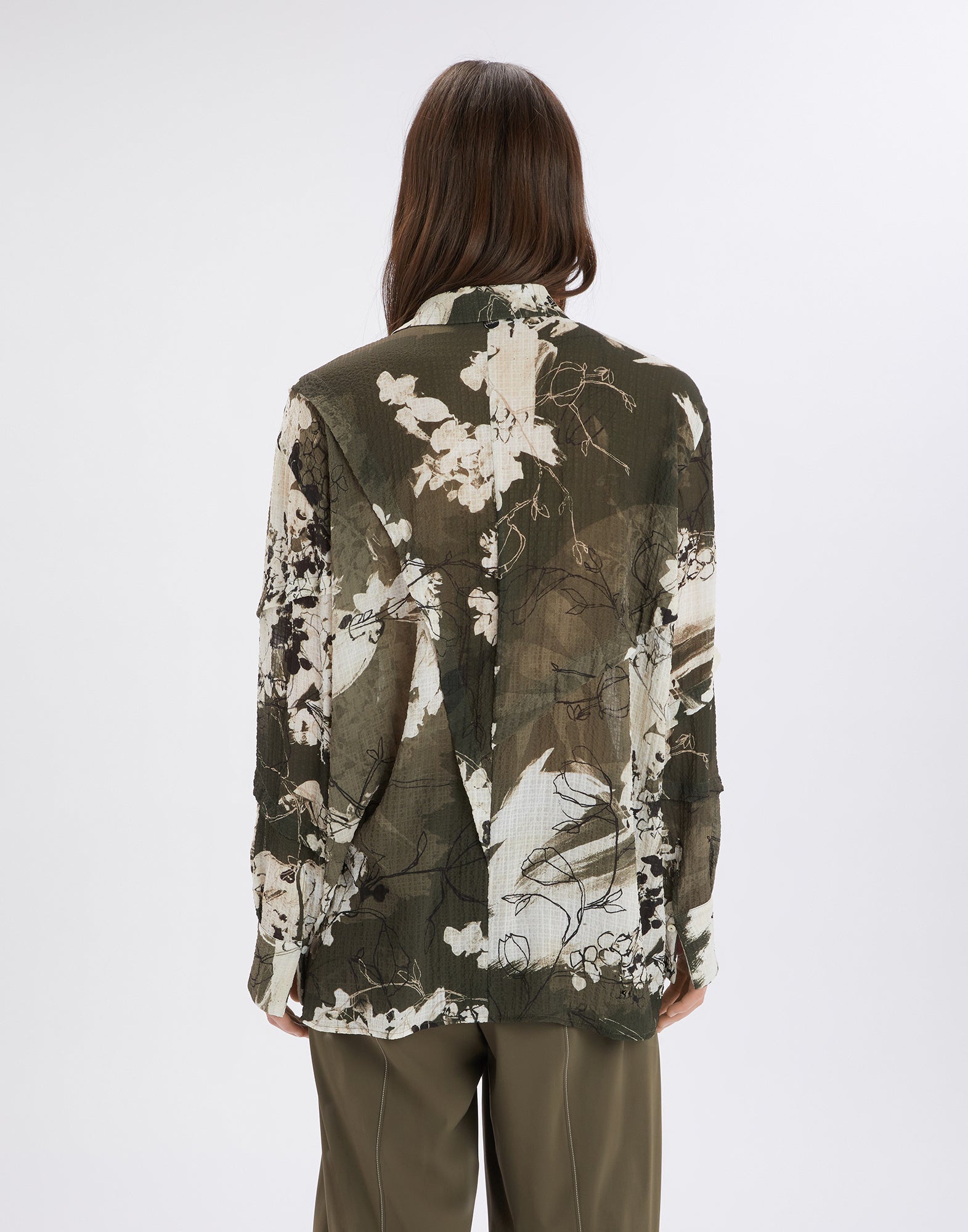 Rear view of a person wearing the oversized WARRANT shirt in green and khaki tones with abstract Layered Flowers pattern. The fabric appears lightly textured.
