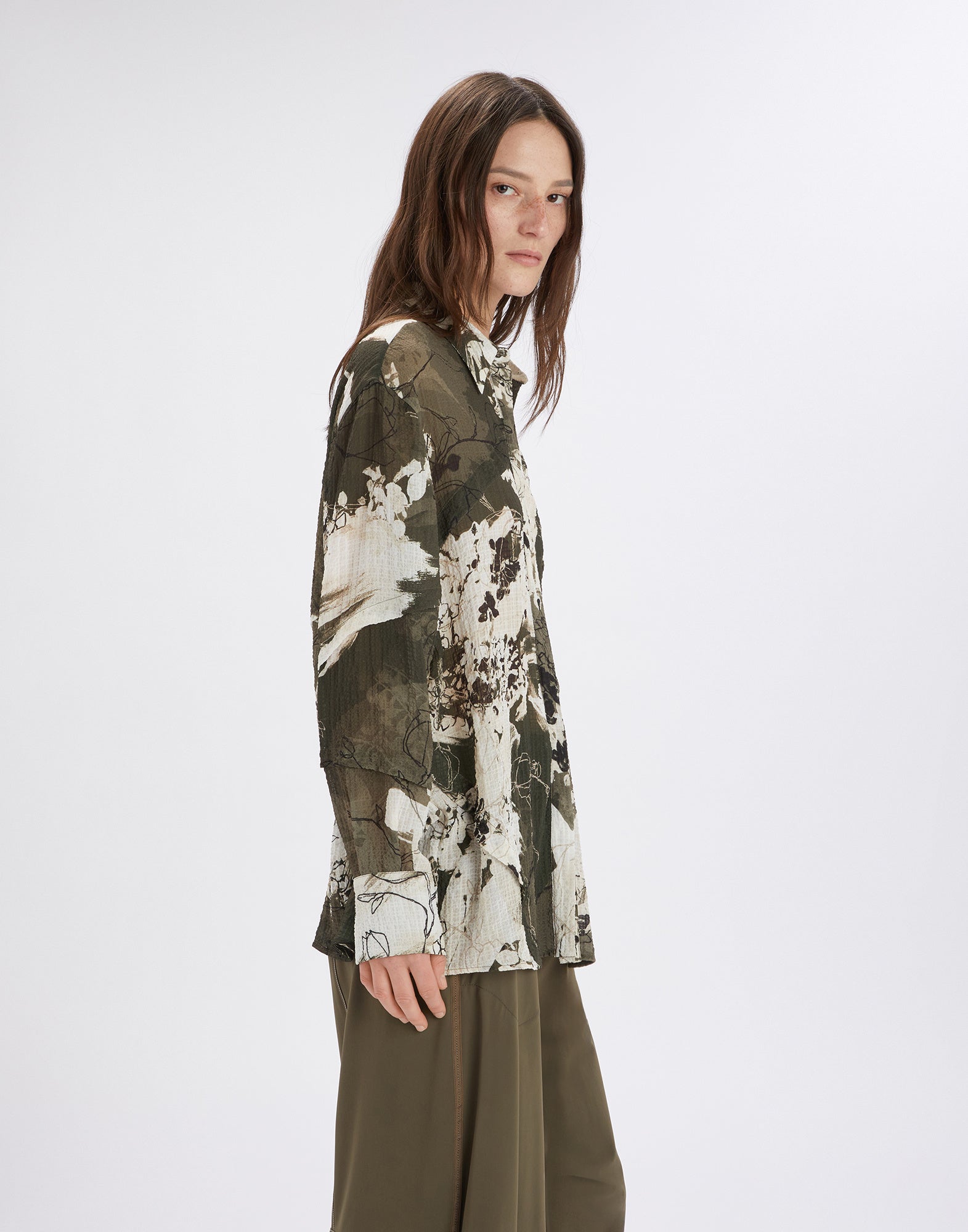 Side view of the WARRANT oversized shirt featuring the 'Layered Flowers' pattern in green and khaki tones, long sleeves, and a classic notched collar.