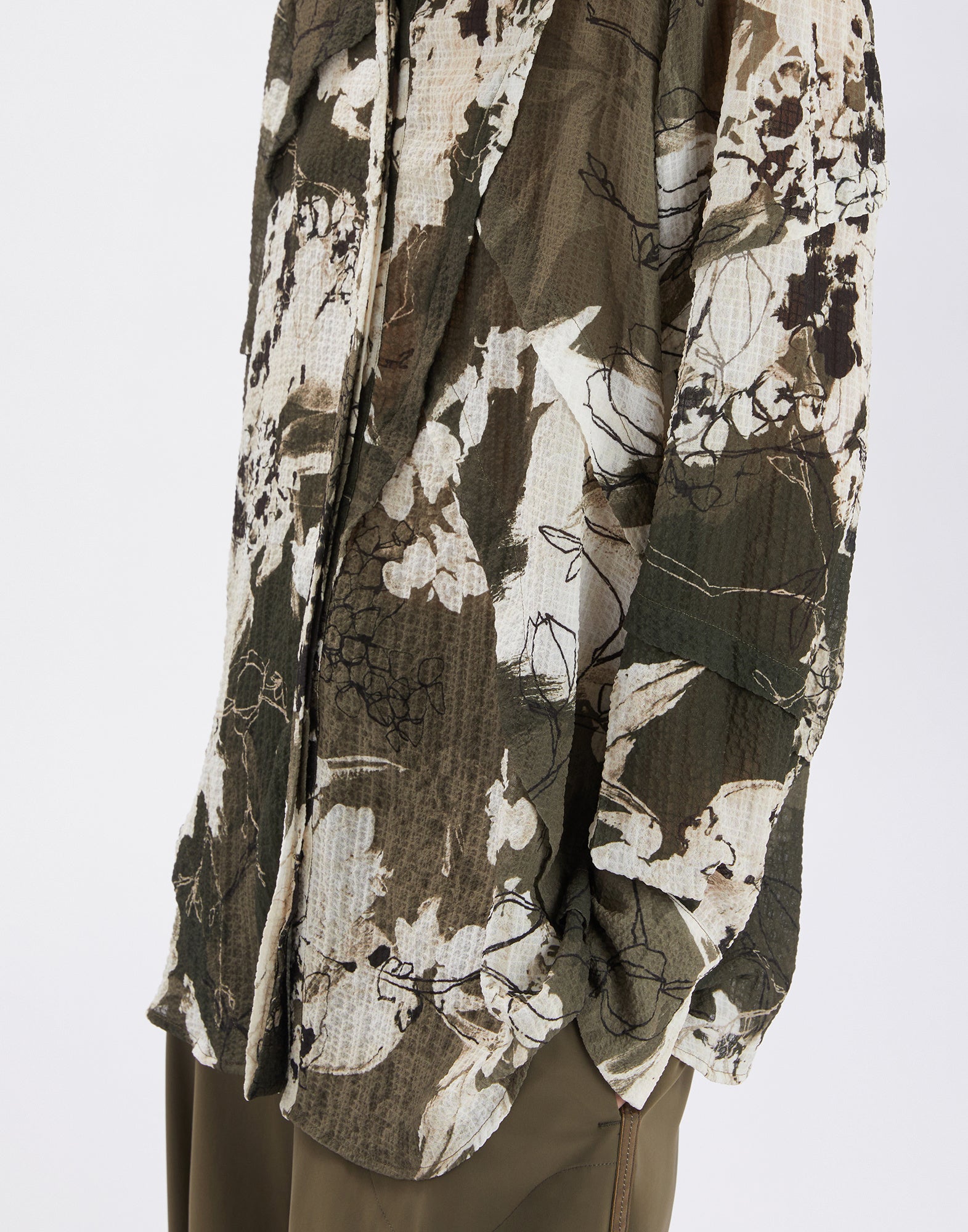 Close-up of the WARRANT shirt with green-khaki artistic Layered Flowers pattern, abstract florals, geometric shapes, and seersucker texture.