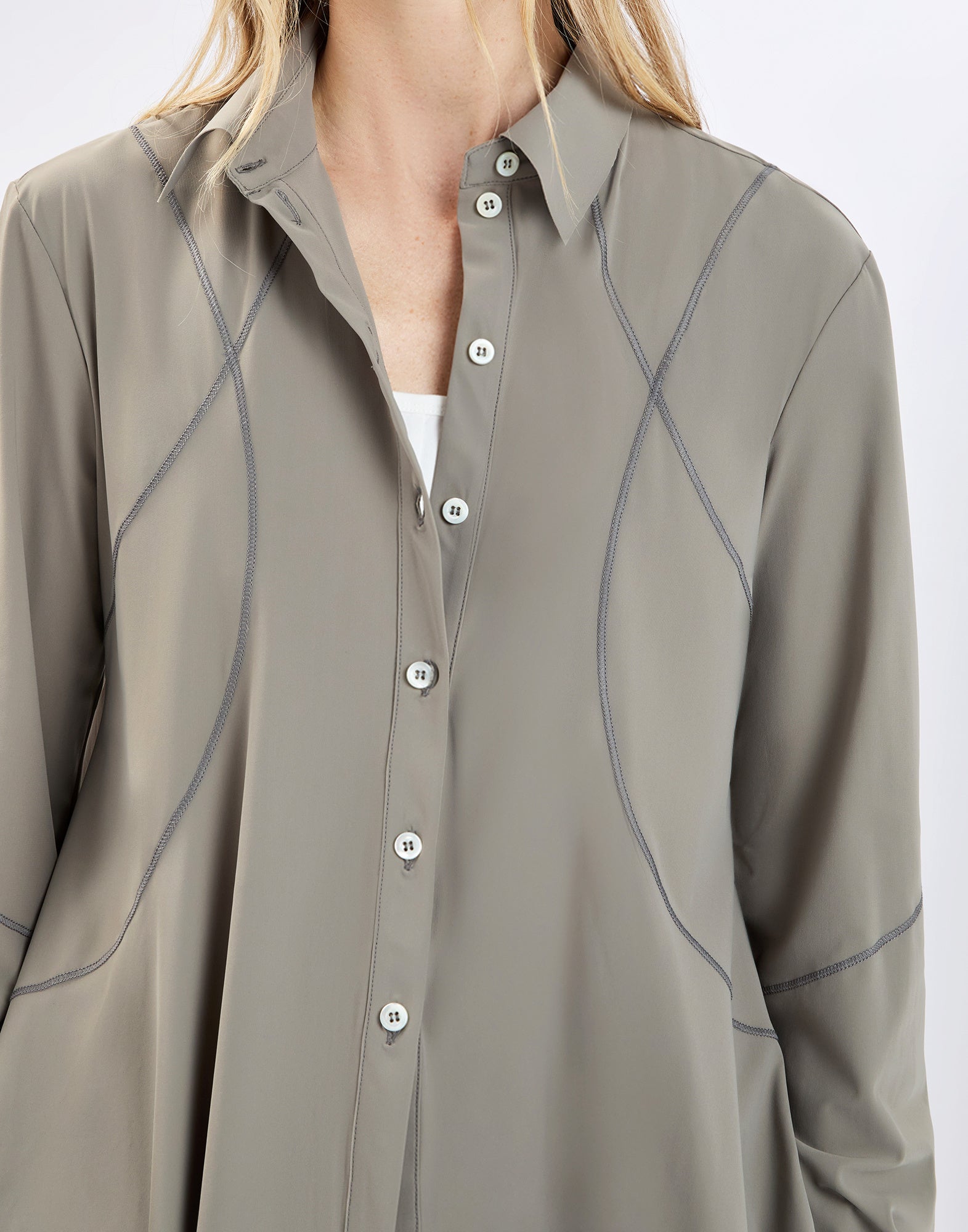 Front view: model wears the DEBONHAIR shirt in taupe, with notched collar, full button placket, visible sporty topstitching and a slightly flared, relaxed fit below the bust.
