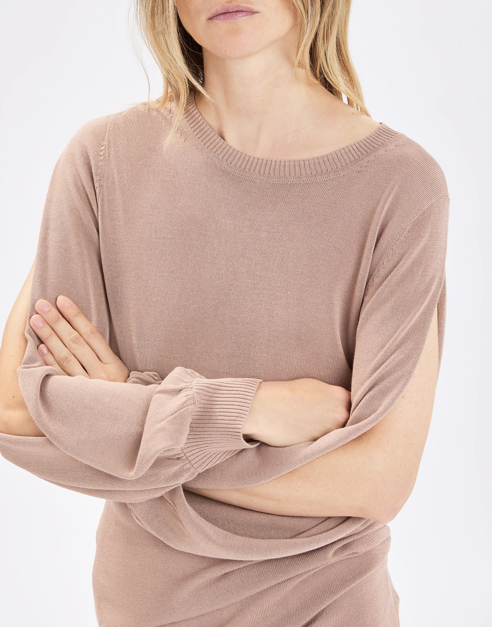Front view: woman wearing the fine knit SANDUST sweater in sand color, with crew neckline, long sleeves with ribbed cuffs and open outer sides that create soft pleats over the arms.