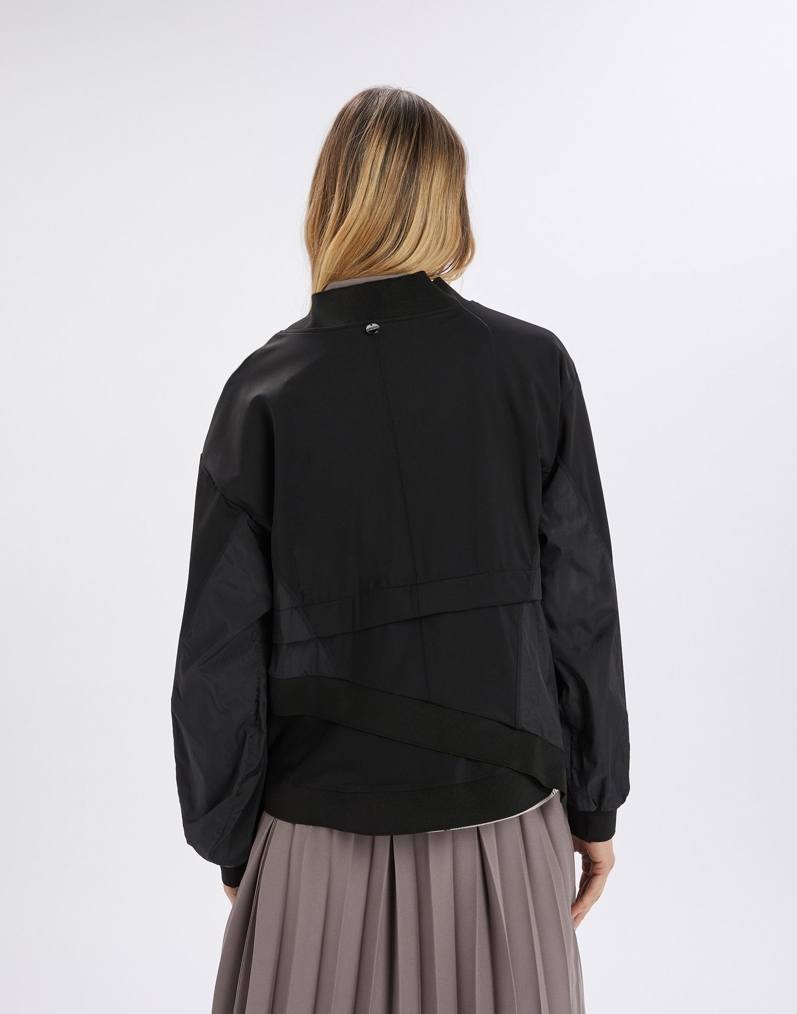 Rear view: person wears the Slink sweatshirt featuring a sculptural silhouette, in black neoprene and nylon, with ribbed collar, cuffs, and asymmetrical hem.