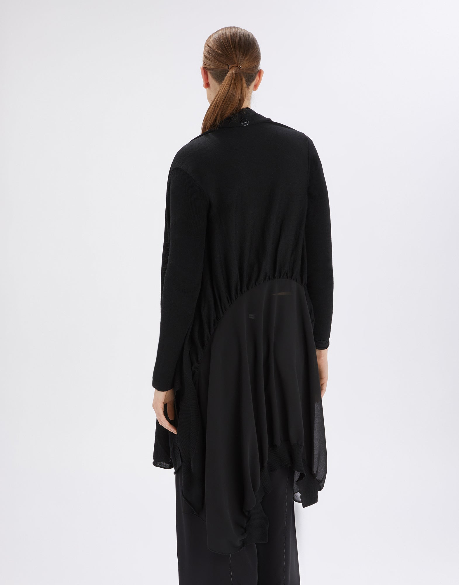 Rückansicht einer Person, die den SLIVER Cardigan trägt; der Cardigan ist schwarz, weit geschnitten, mit gerafftem Rückenteil und unregelmäßigem Saum, lange Ärmel.