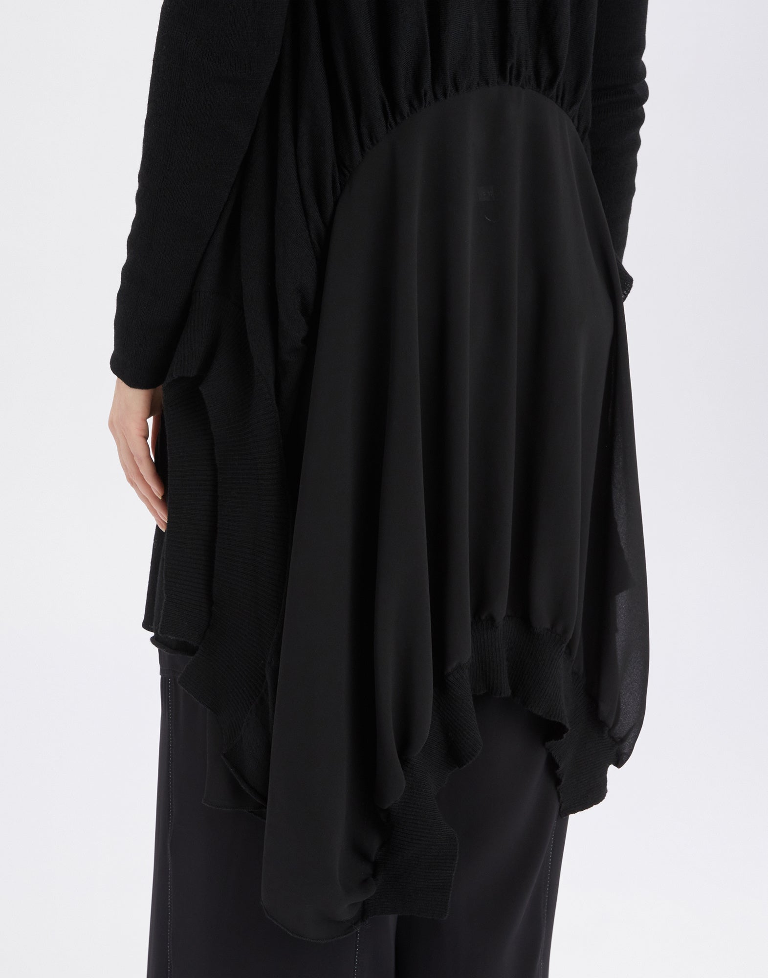 Detailansicht des SLIVER Cardigans, die die geraffte Rückseite und den abgerundeten, unregelmäßigen Saum mit gerippten Bündchen aus schwarzer Wollmischung zeigt.