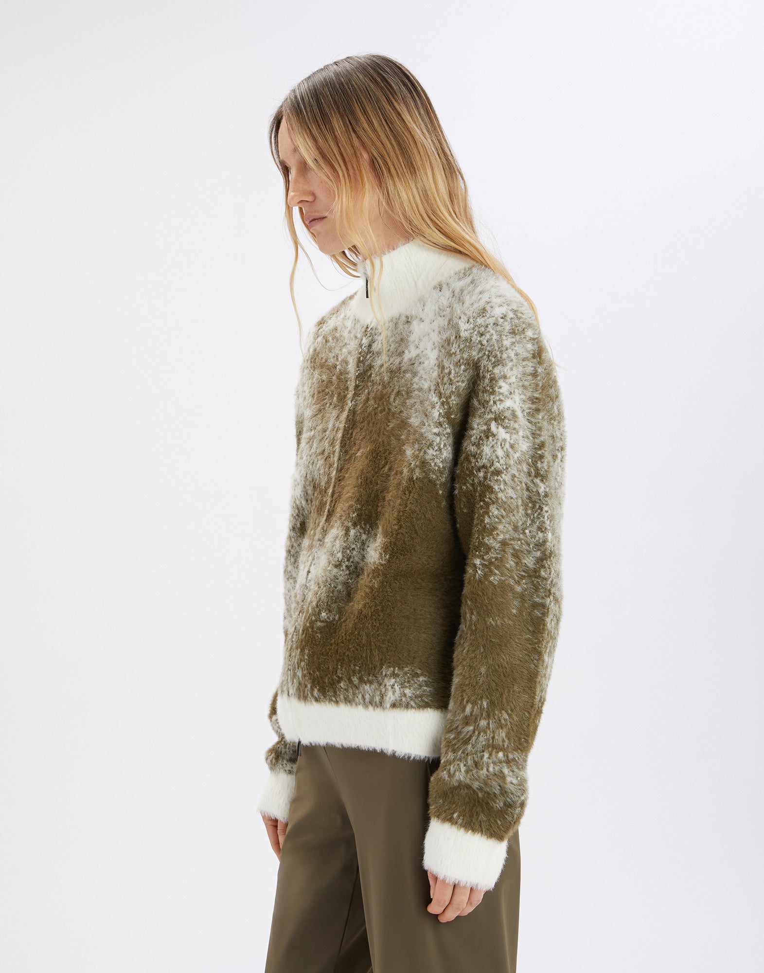 Seitenansicht einer Person, die den SUMMON UP Cardigan trägt; locker geschnitten mit bicolor Jacquard in Olivgrün und Creme, sichtbarer Stehkragen und farblich abgesetzte Bündchen.